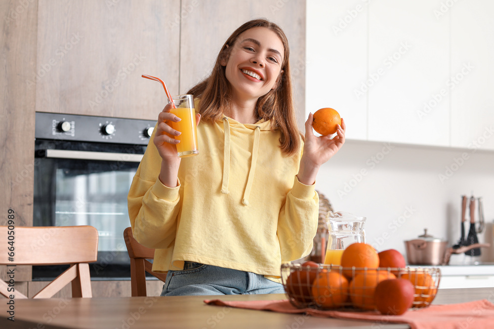 Young woman with glass of juice and orange in kitchen