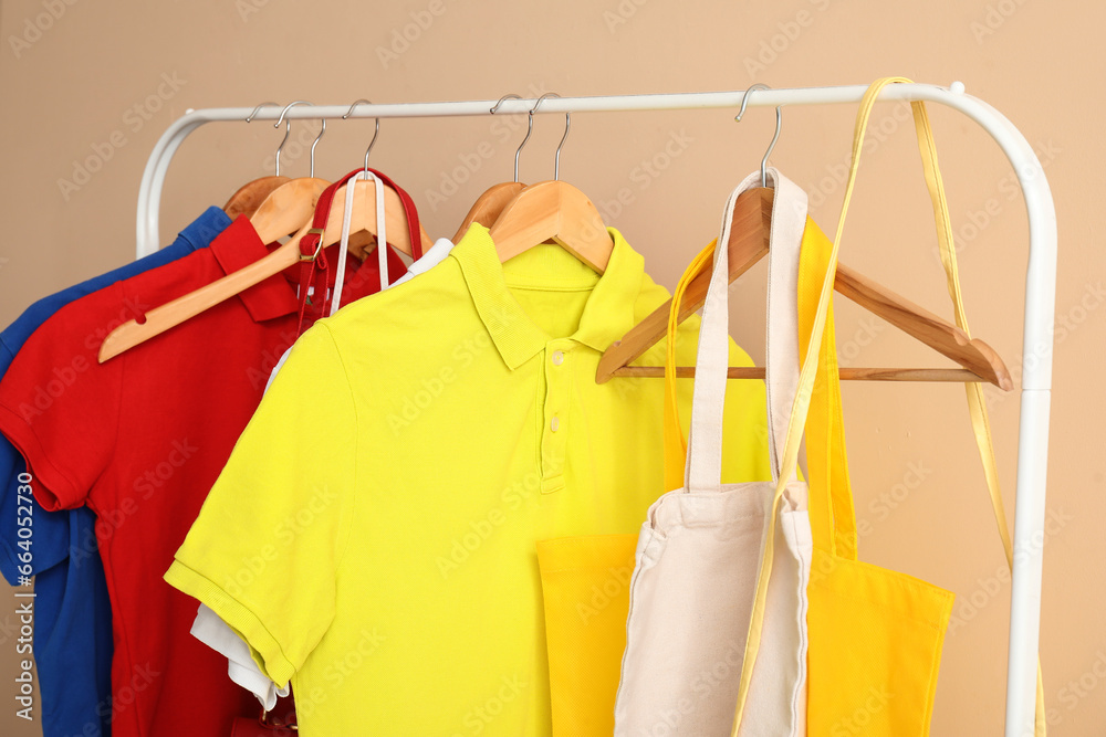 Rack with different clothes and bags near color wall, closeup