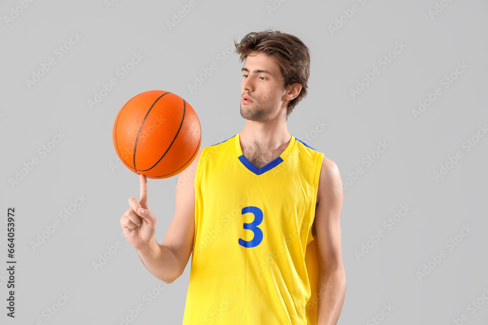 Portrait of young basketball player in yellow uniform holding ball on grey background