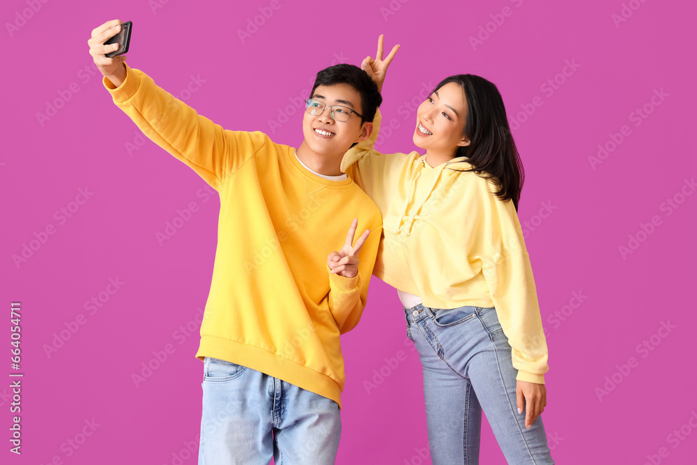 Young Asian friends taking selfie on violet background