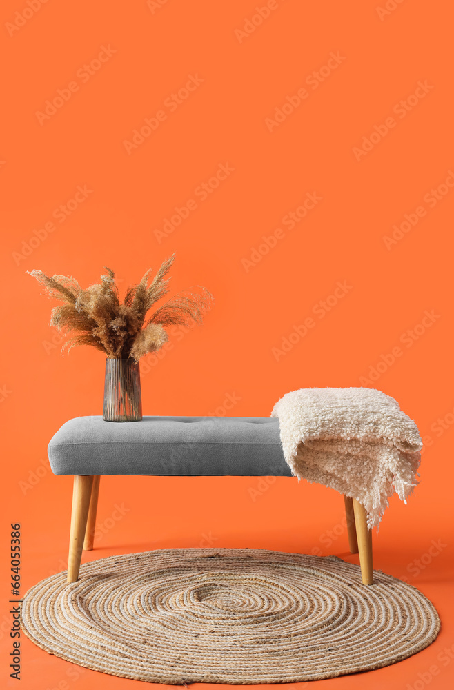 Vase with pampas grass on soft bench against orange background