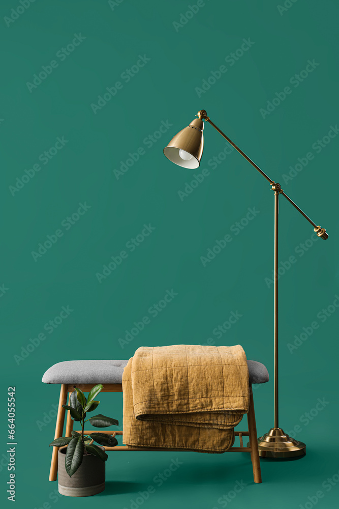 Soft bench with plaid, plant and lamp on green background