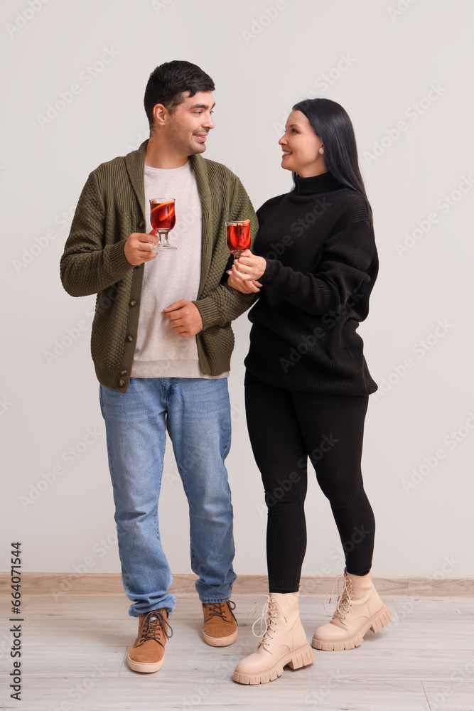 Young couple with glasses of mulled wine near light wall