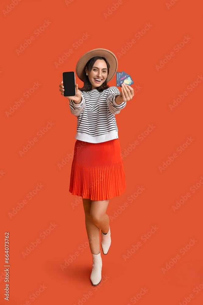 Beautiful young woman with mobile phone and credit cards on red background