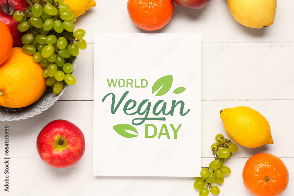 Card with text WORLD VEGAN DAY and basket of fresh fruits on white wooden background