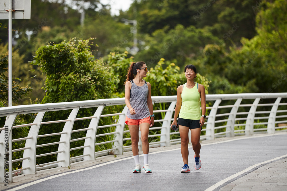 two young asian joggers athletes walking relaxing chatting outdoors in park