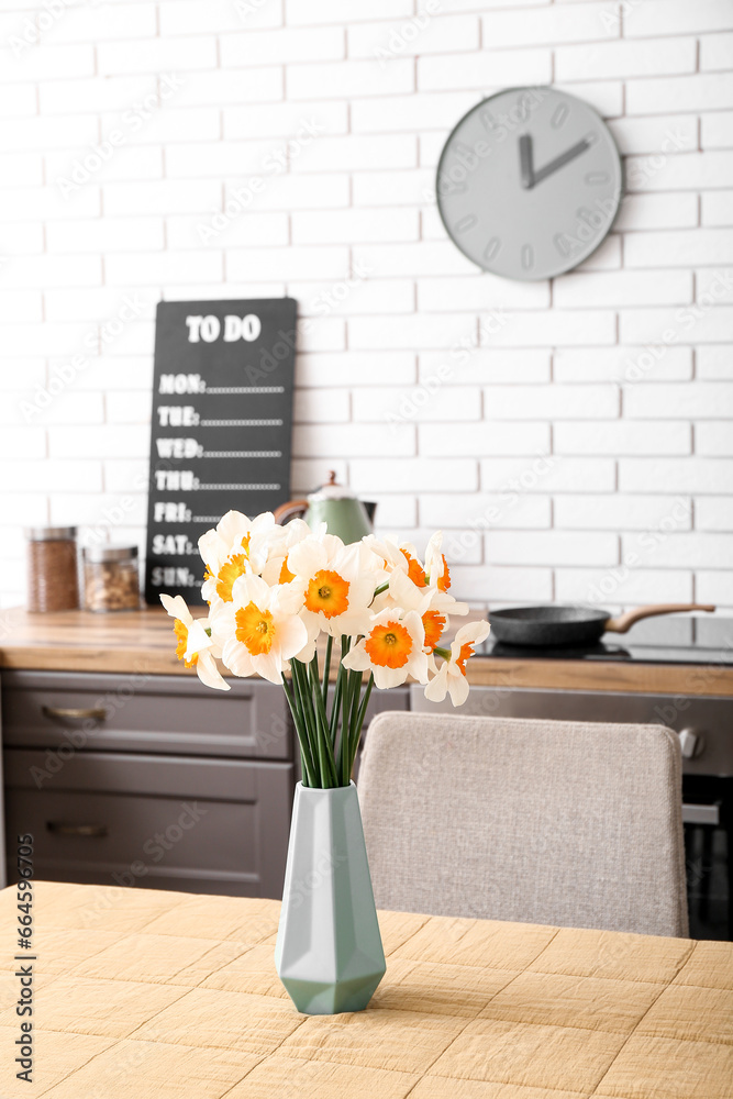 Vase with blooming narcissus flowers on table in modern kitchen