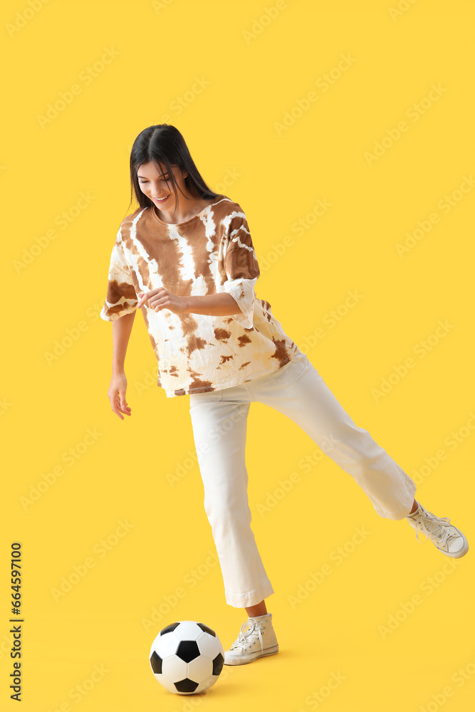 Young woman playing with soccer ball on yellow background