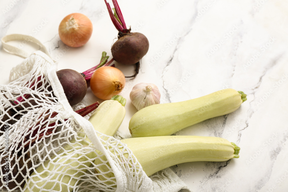 Mesh bag with different fresh vegetables on light background, closeup