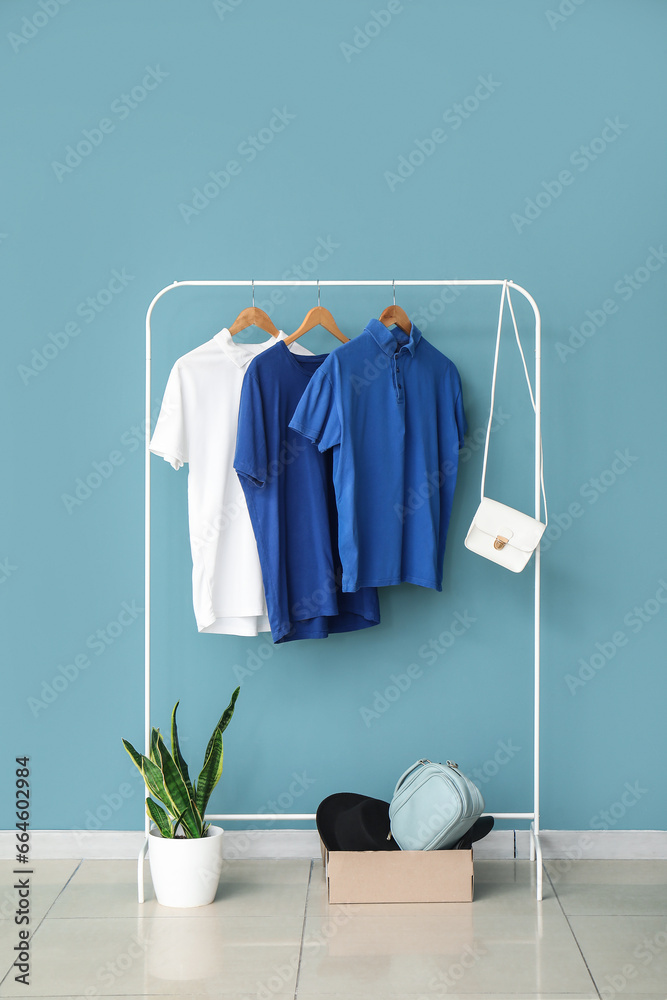 Rack with stylish clothes, accessories and houseplant near color wall