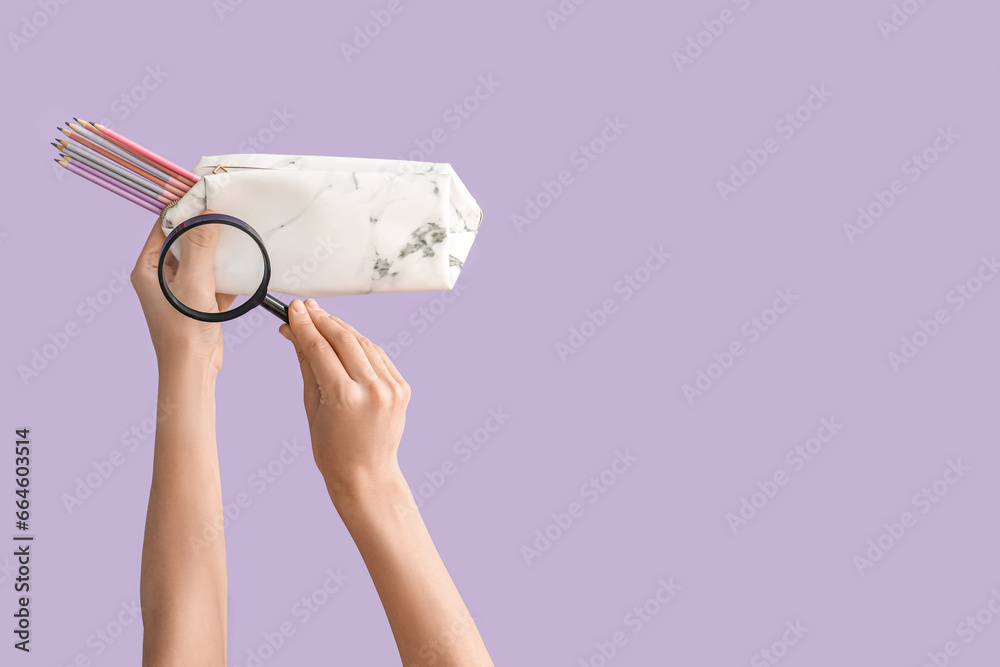 Female hands holding pencil case and magnifying glass on lilac background