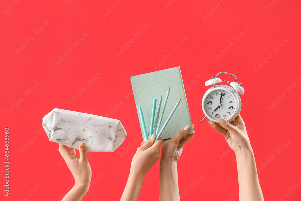 Hands with set of stationery and alarm clock on red background