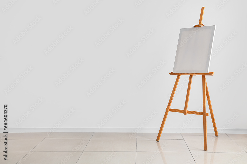 Wooden easel with blank canvas near grey wall