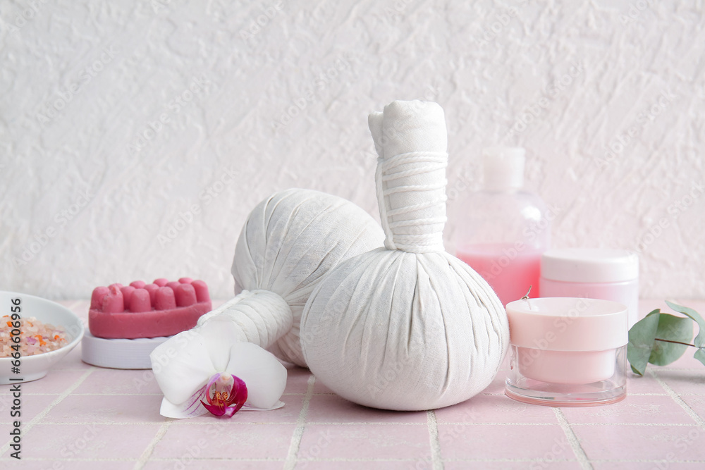 Composition with herbal massage bags and cosmetic products on color tile background