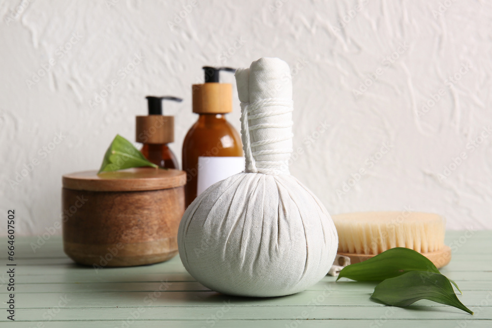 Cosmetic products, herbal massage bag and brush on color wooden table near light wall