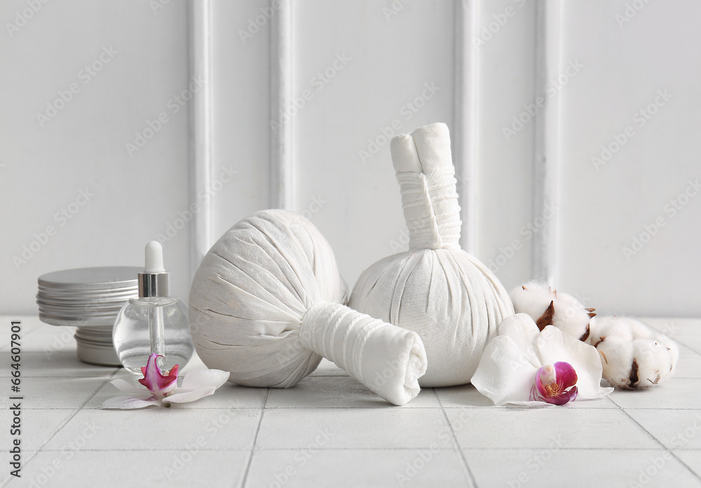 Herbal massage bags, cosmetic products and flowers on light tile table