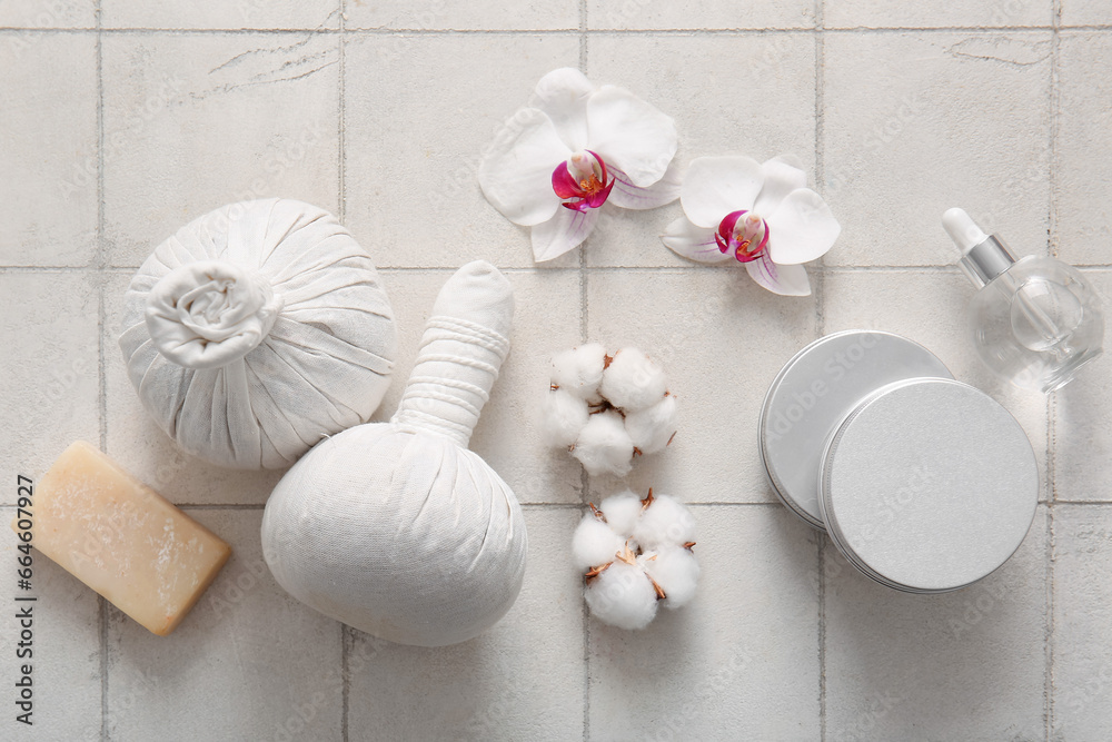 Composition with cosmetic products, herbal massage bags and flowers on light tile background