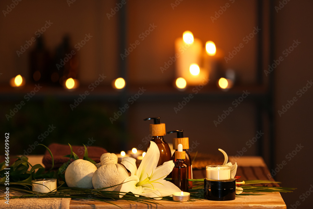 Spa composition with lily flowers and burning candles on table in dark salon, closeup