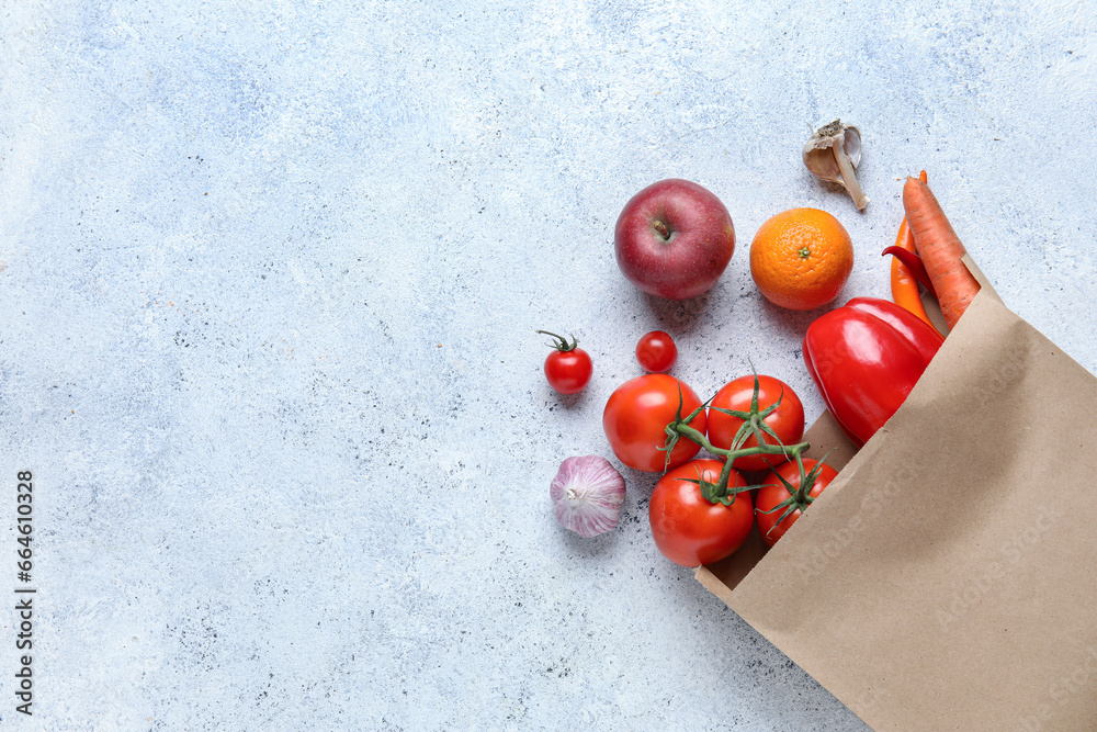 Paper bag with fruits and vegetables on light blue background