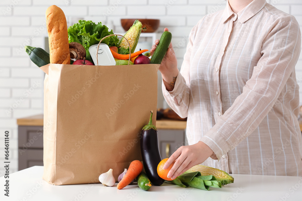 Woman and paper bag with different products on table in kitchen