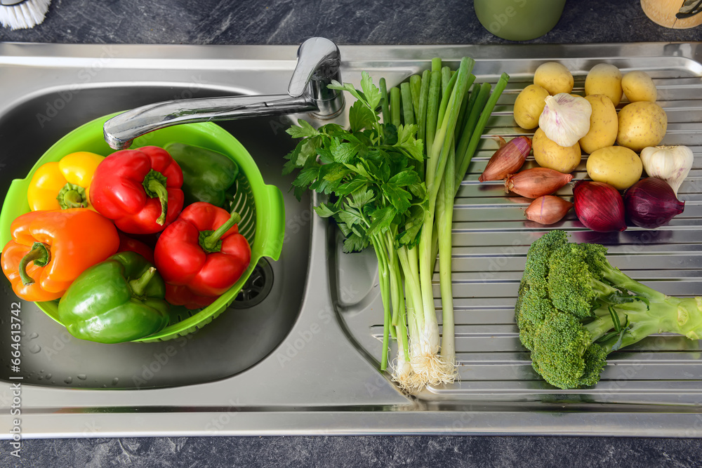 Colander with peppers and fresh vegetables on metal sink