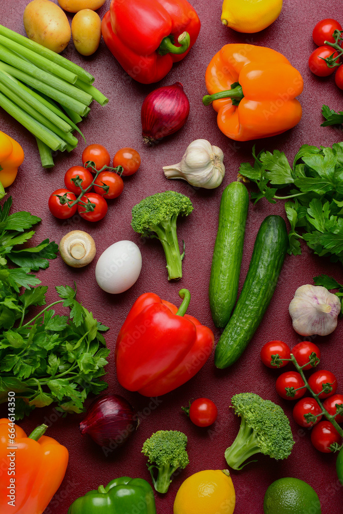 Fresh vegetables, greenery and fruits on burgundy background