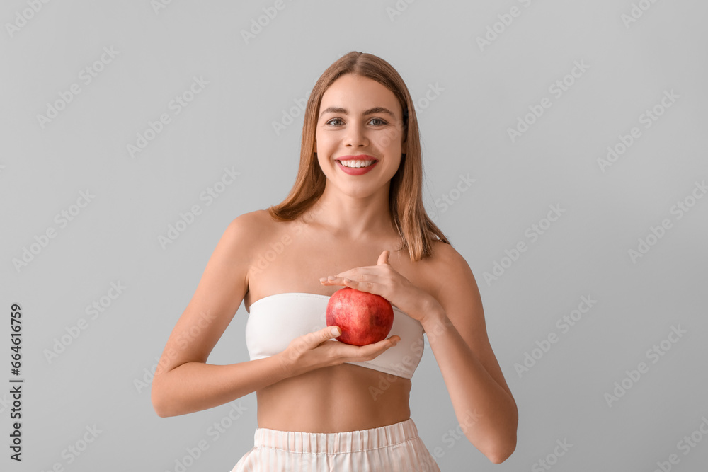 Young woman with pomegranate on light background