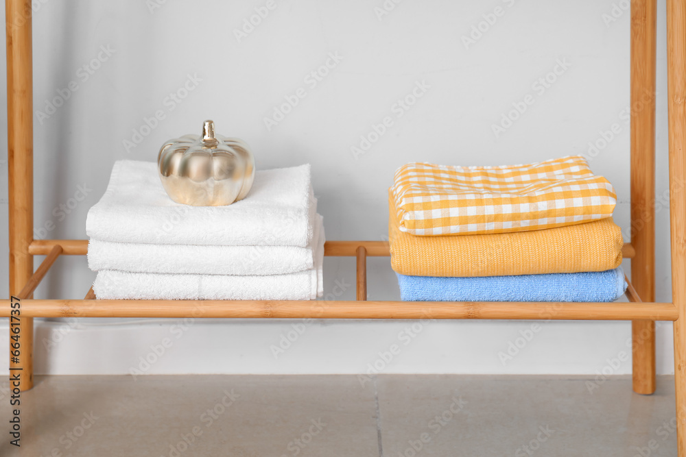 Rack with clean towels and decor near light wall