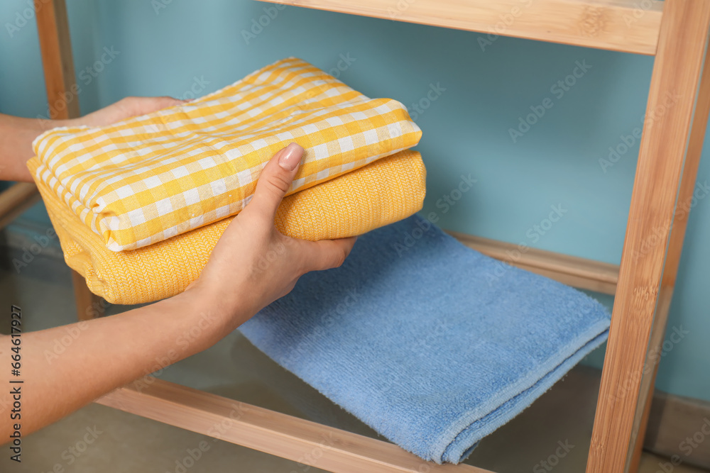 Woman putting clean laundry on shelving unit near color wall, closeup