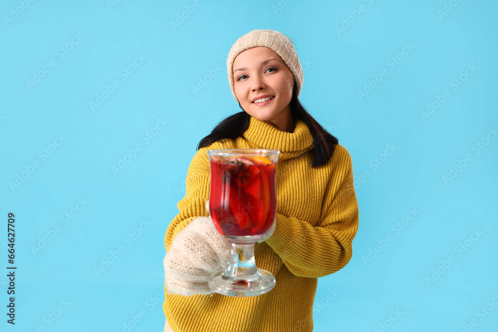 Young woman with glass of mulled wine on blue background