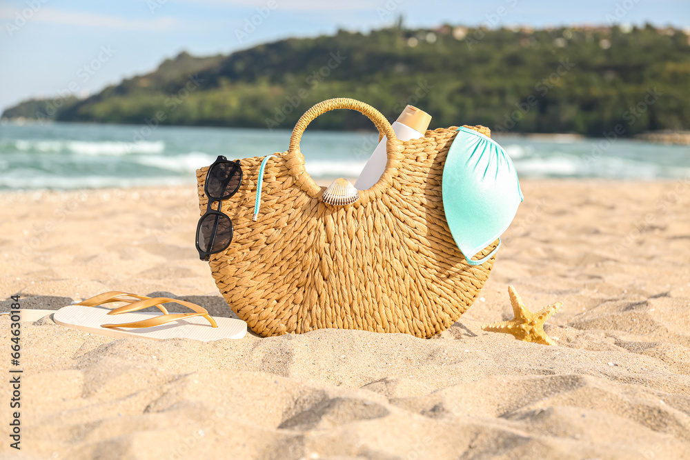 Straw bag with bottle of sunscreen cream and swimsuit on sand