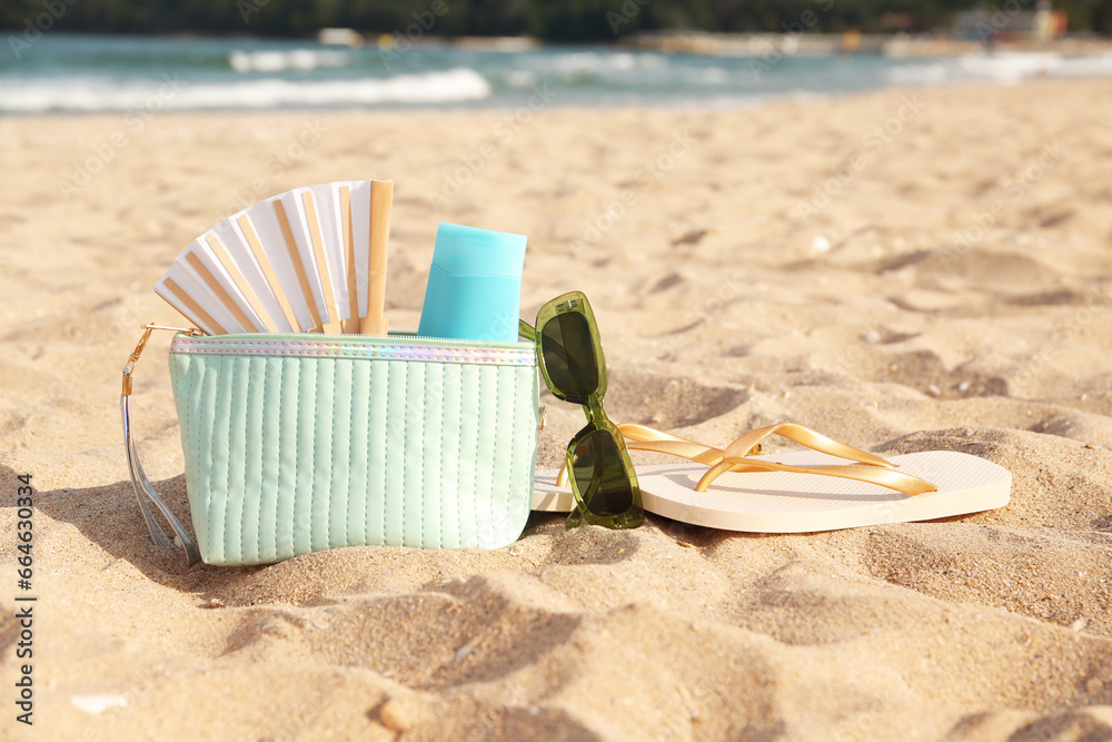 Cosmetic bag with bottle of sunscreen cream and flip flops on sand