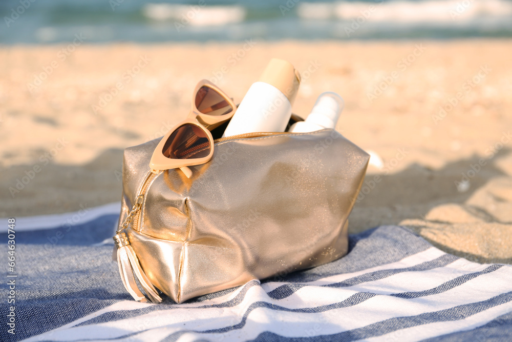 Cosmetic bag with bottles of sunscreen cream and sunglasses on sand