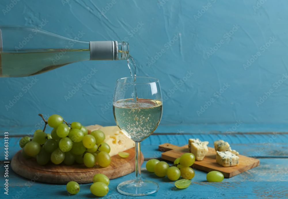 White wine pouring into glass and boards with grape on blue wooden table