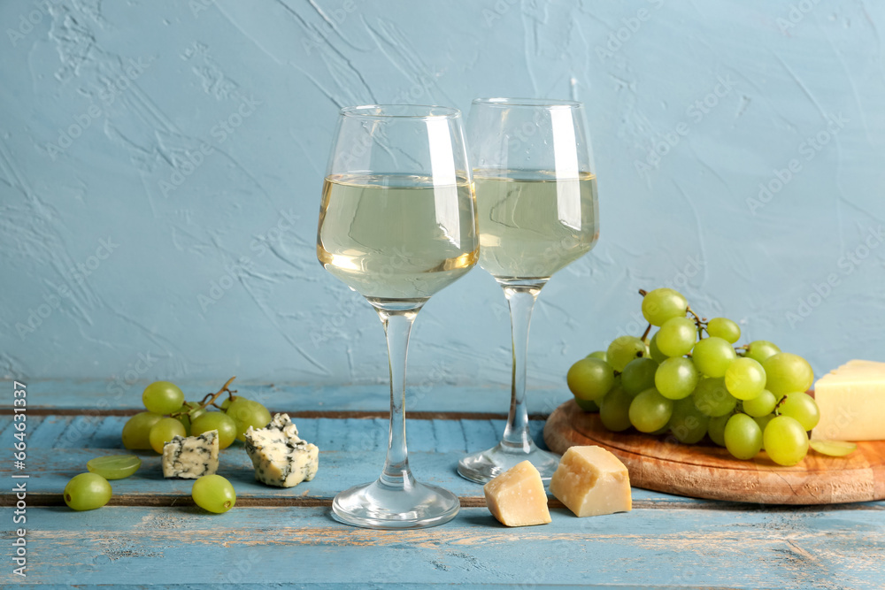 Glasses of tasty wine with grape and cheese on blue wooden table