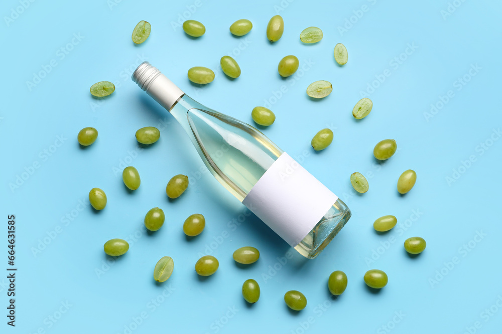 Bottle of tasty wine with blank label and grape on blue background