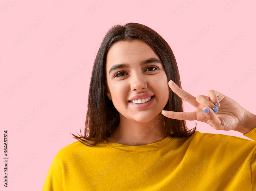 Smiling young woman with healthy teeth showing victory gesture on pink background, closeup