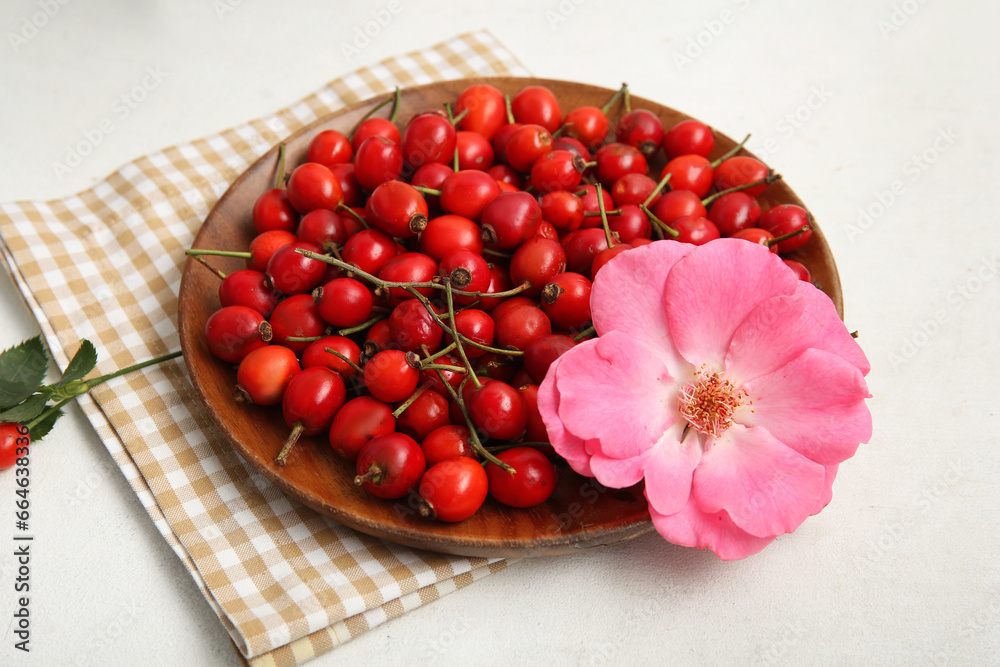 Wooden plate with fresh rose hip berries and flower on white background