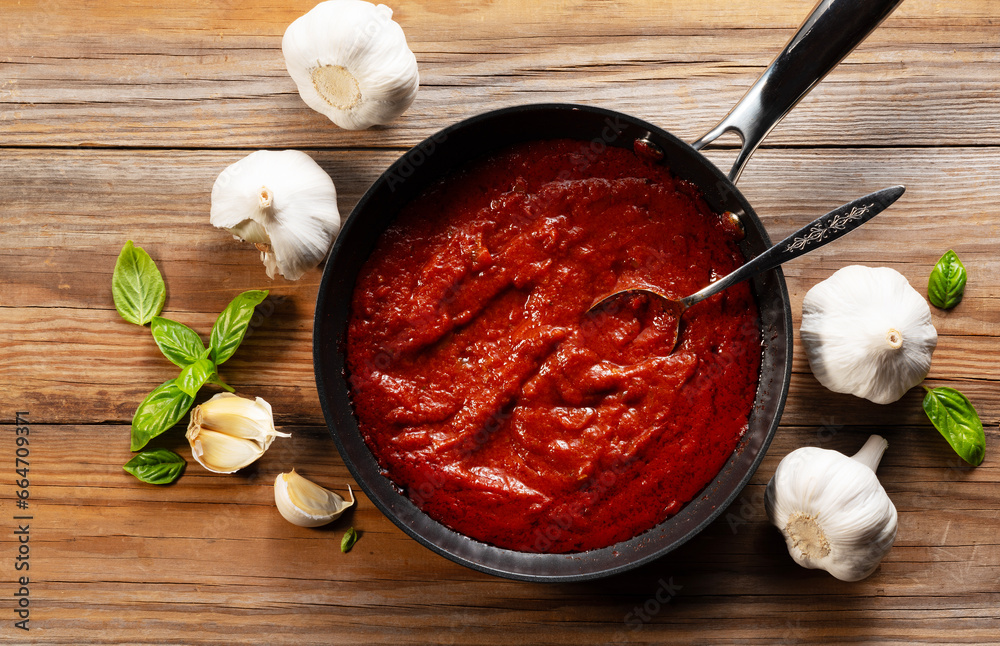 Tomato sauce in a frying pan. Basil and garlic around. View from directly above.