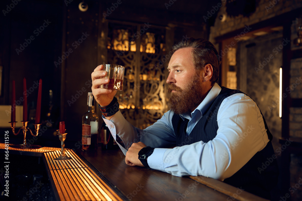 Young adult man in bar drinking whiskey from glass