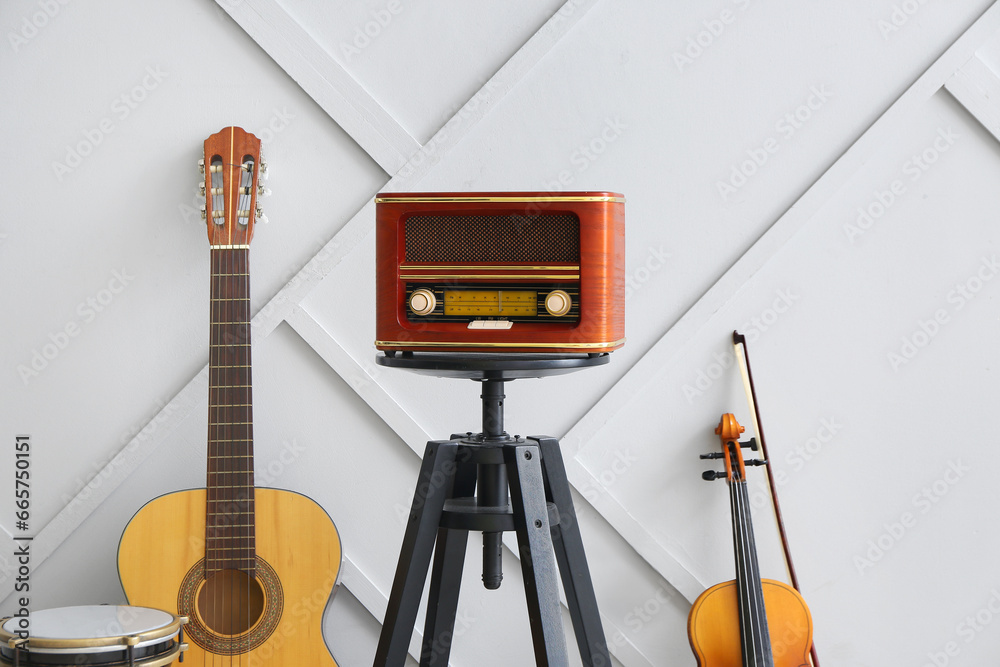 Retro radio receiver and different musical instruments near light wall