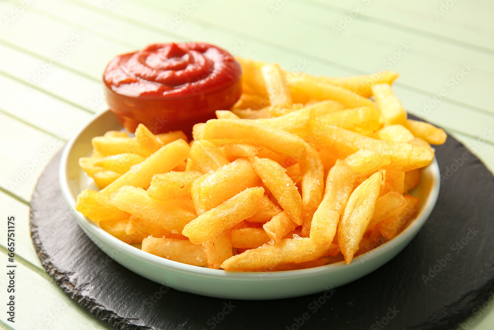 Plate with tasty french fries and bowl of ketchup on color wooden background, closeup