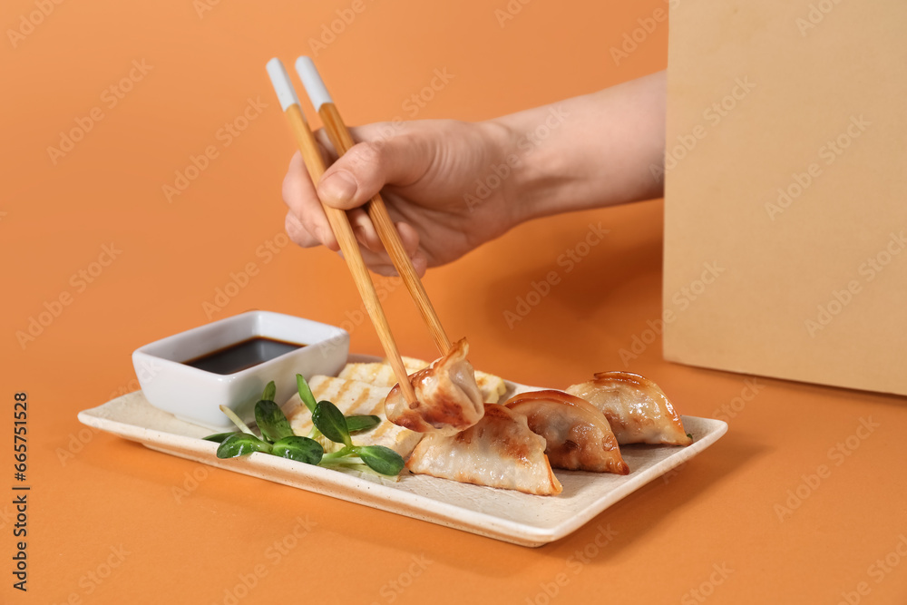 Female hand with chopsticks, Chinese dumplings, tofu cheese and soy sauce on color background, closeup