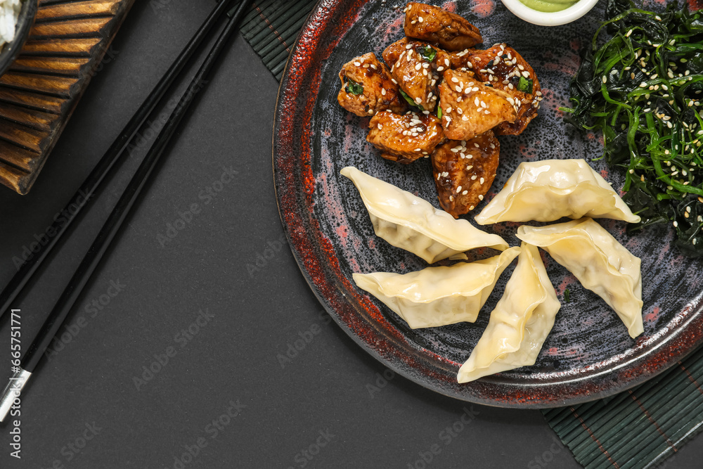 Plate with tasty Chinese dishes and chopsticks on dark background, closeup