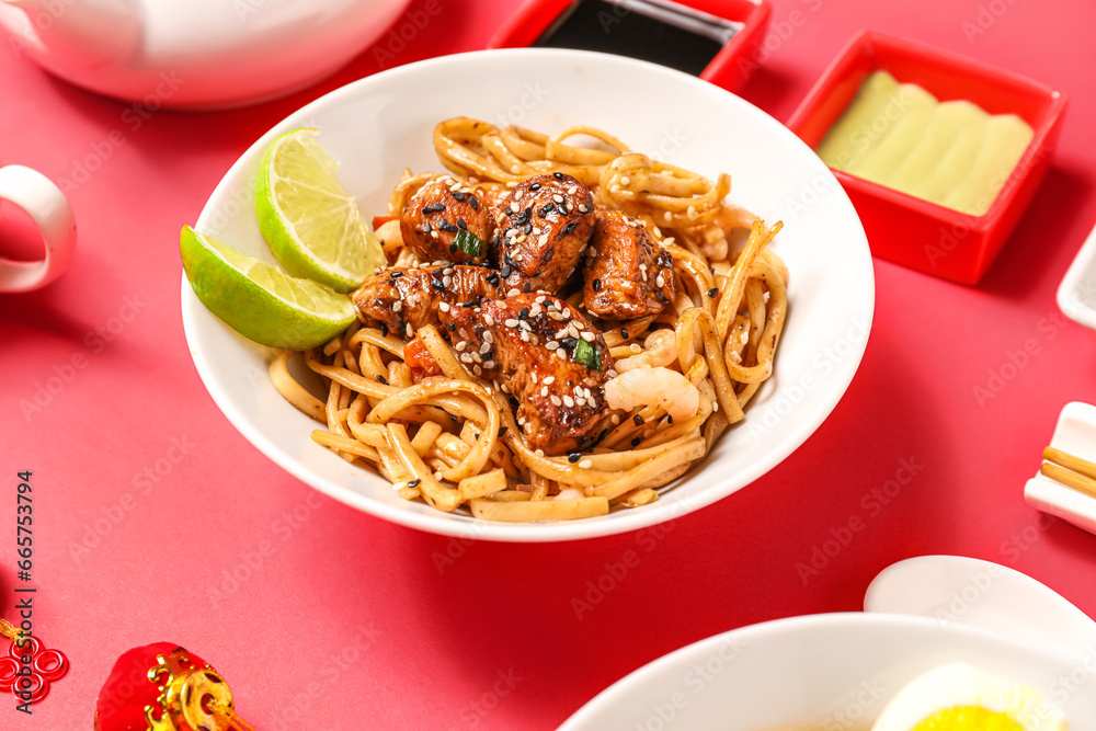 Bowl with tasty Chinese noodles with chicken and sauces on red background