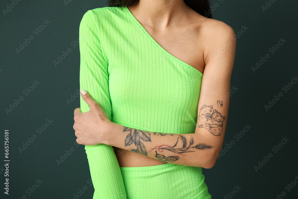 Young woman with tattooed arm on green background, closeup