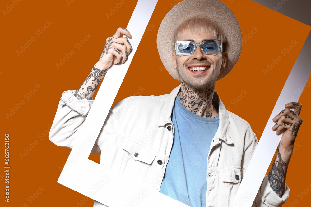 Young tattooed man in stylish sunglasses with frame on color background