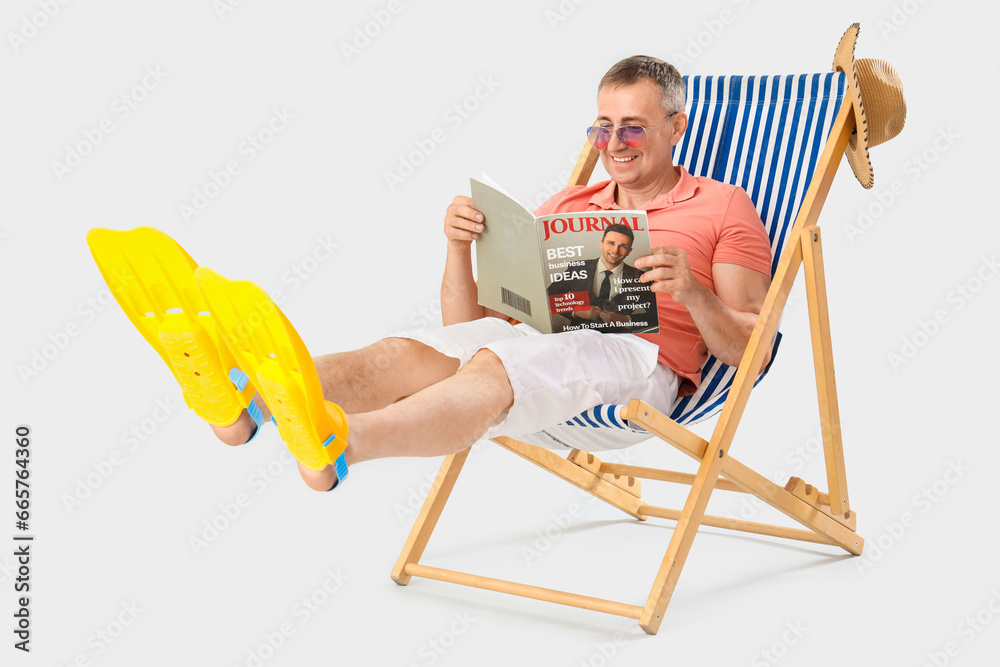 Mature man reading magazine in deck chair on light background