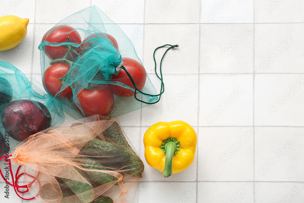 Eco bags with different fresh vegetables on light tile background