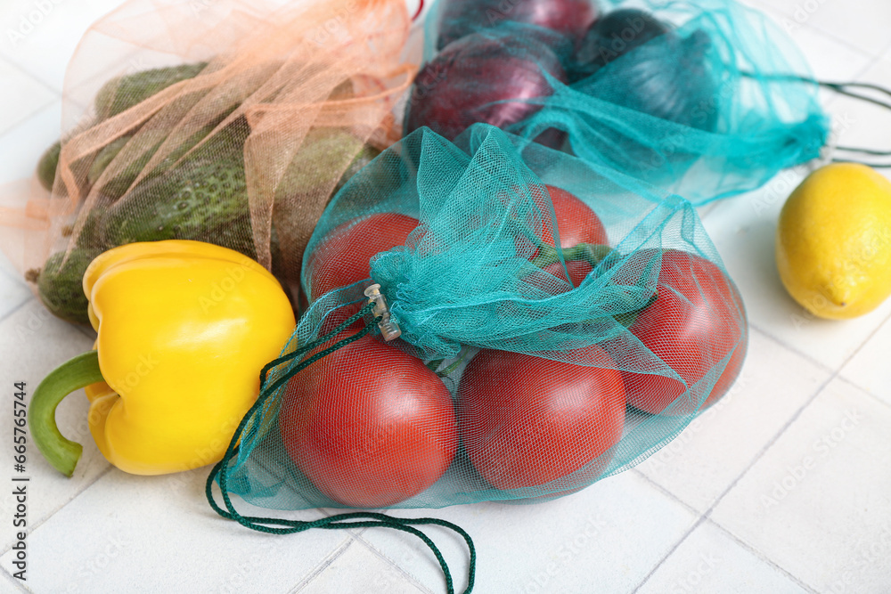 Eco bags with different fresh vegetables on light tile background, closeup